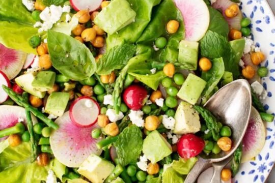Colorful bowl of salad with greens, nuts, and fruits.